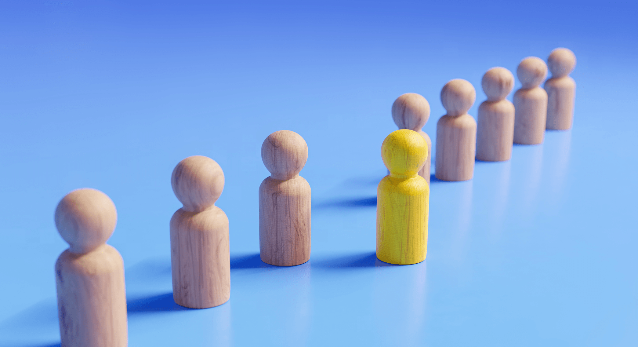 Holzfiguren stehen in einer diagonalen Reihe vor einem blauen Hintergrund, wobei eine gelbe Figur einen Schritt voraus ist.