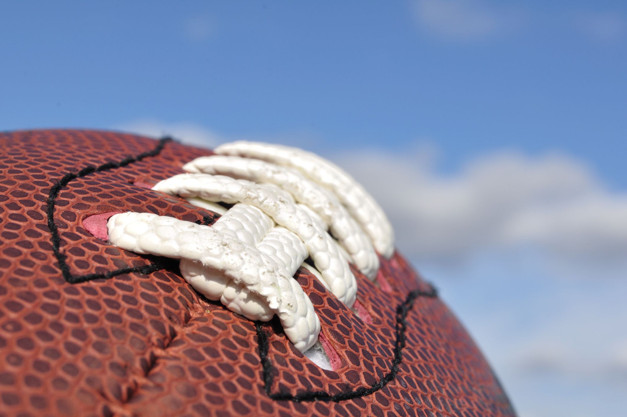 Nahaufnahme eines braunen Footballs mit weißen Schnürsenkeln und blauem Himmel im Hintergrund.