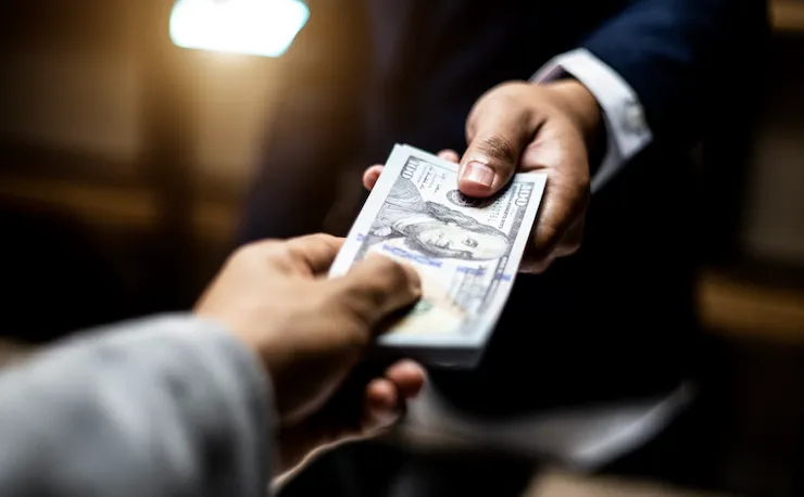 Nahaufnahme der Hand eines Geschäftsmannes, der einem anderen ein Bündel aus 100 -Dollar-Scheinen überreicht
