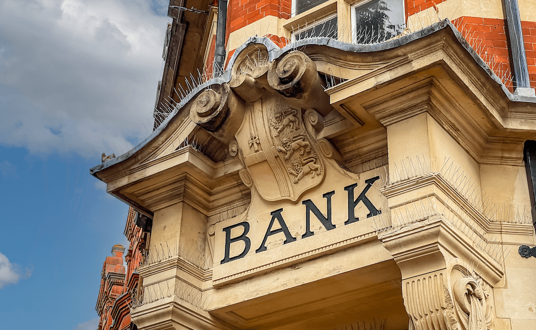 Die Steinfassade einer britischen Bank mit kunstvollen Verzierungen und dem Wort „Bank“ über dem Eingang eingraviert.