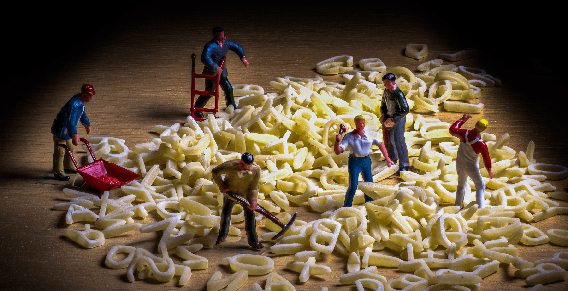 Ein Foto von Miniaturfiguren, die Arbeiter mit Spitzhacken und Schubkarren darstellen, die in einem Haufen von Buchstaben aus der „Buchstabensuppe“ graben.