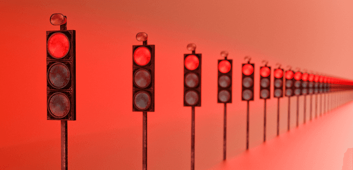 A row of traffic lights, all lit red, trail off into the distance.