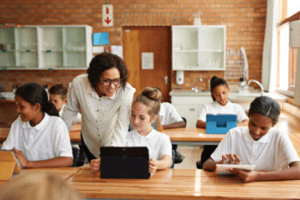 Lehrer, der Schülern am Pult mit einem Tablet-Computer im Klassenzimmer hilft