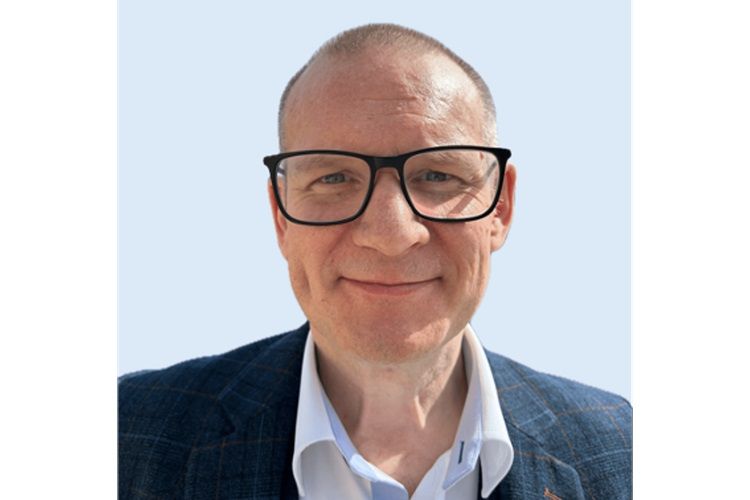 Abbildung eines weißen Mannes mit kurzgeschnittenem Haar und einer Brille mit großem Rahmen, der eine graue karierte Jacke trägt.