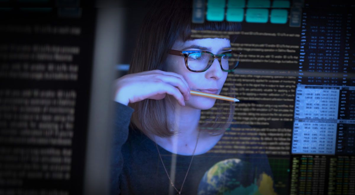Berufstätige Frau in blauem Blazer, die Datenkabel in der Hand hält, vor dem Hintergrund eines Serverraums
