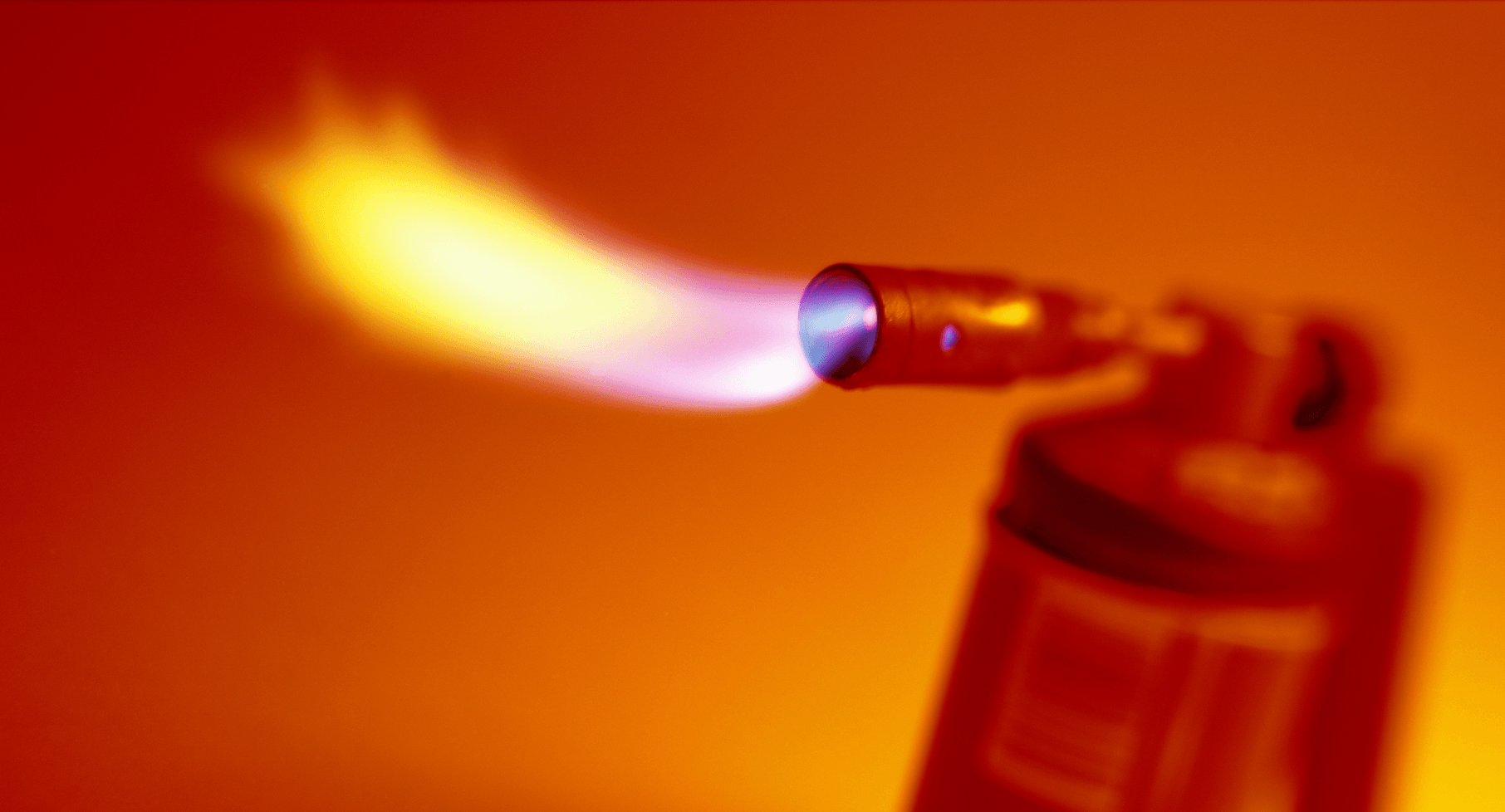 Ein Foto eines roten Schweißbrenners, der Flammen speit, vor einem orangefarbenen Hintergrund.