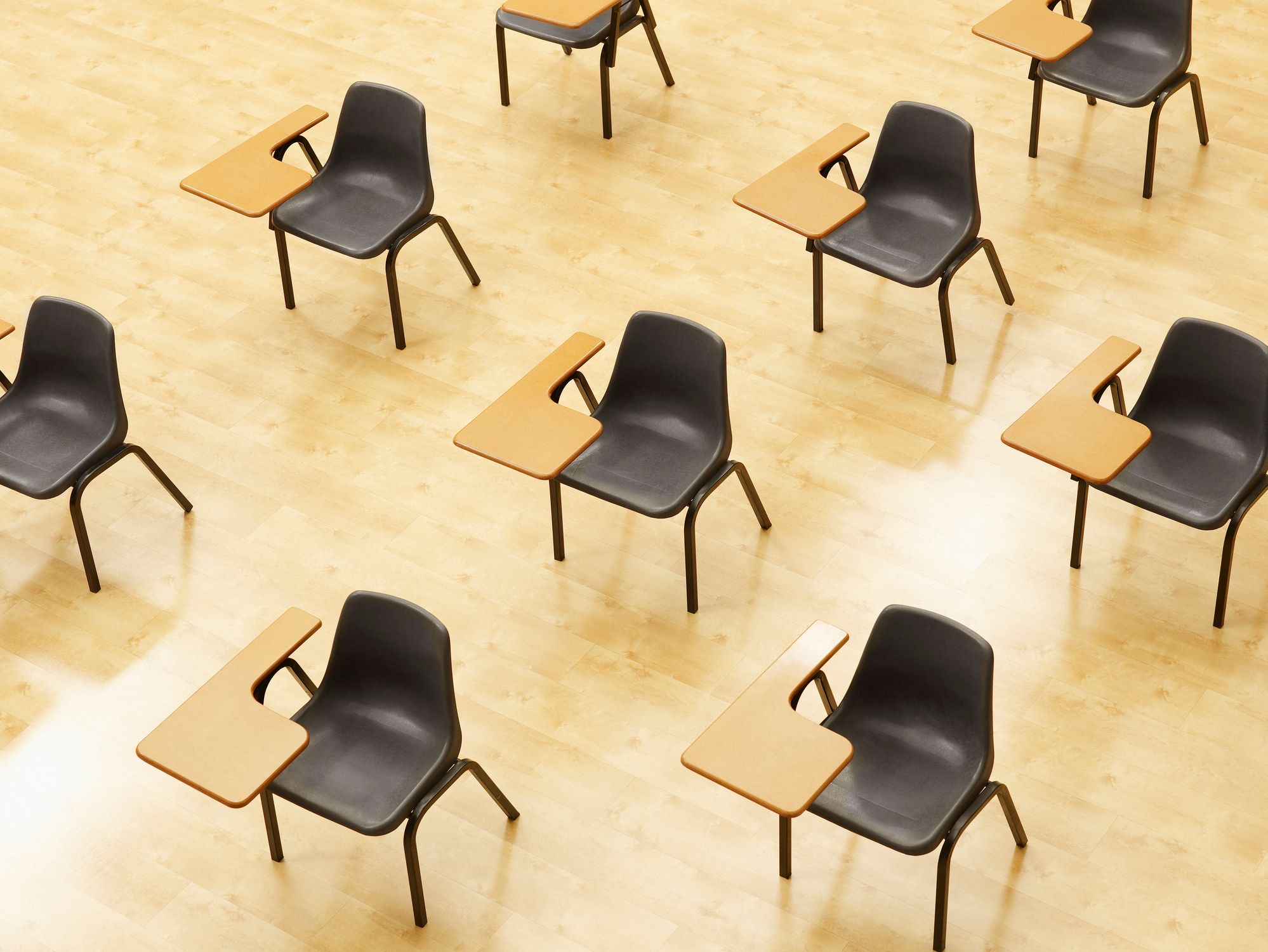Reihen von Schreibtischen stehen diagonal in einem leeren Klassenzimmer.