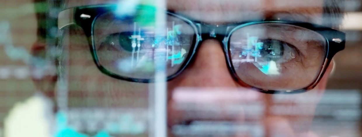 Stockbild: Mann mit Brille, der Diagramme auf einem transparenten Bildschirm betrachtet
