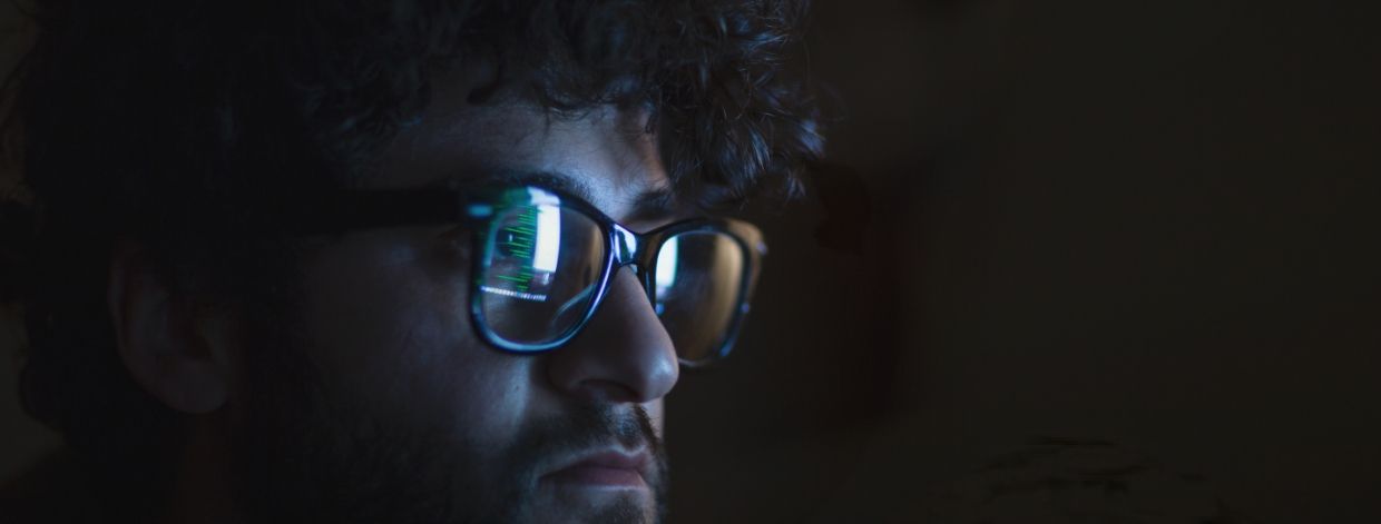 Stockfoto: Gesicht in einem dunklen Raum, beleuchtet vom Schein eines Computerbildschirms