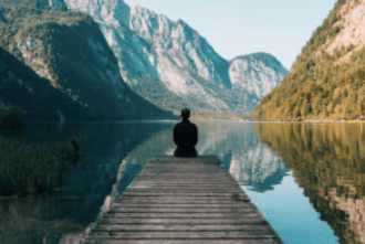 Eine Person sitzt auf einem Steg mit Blick auf einen Bergsee und eine bewaldete Landschaft