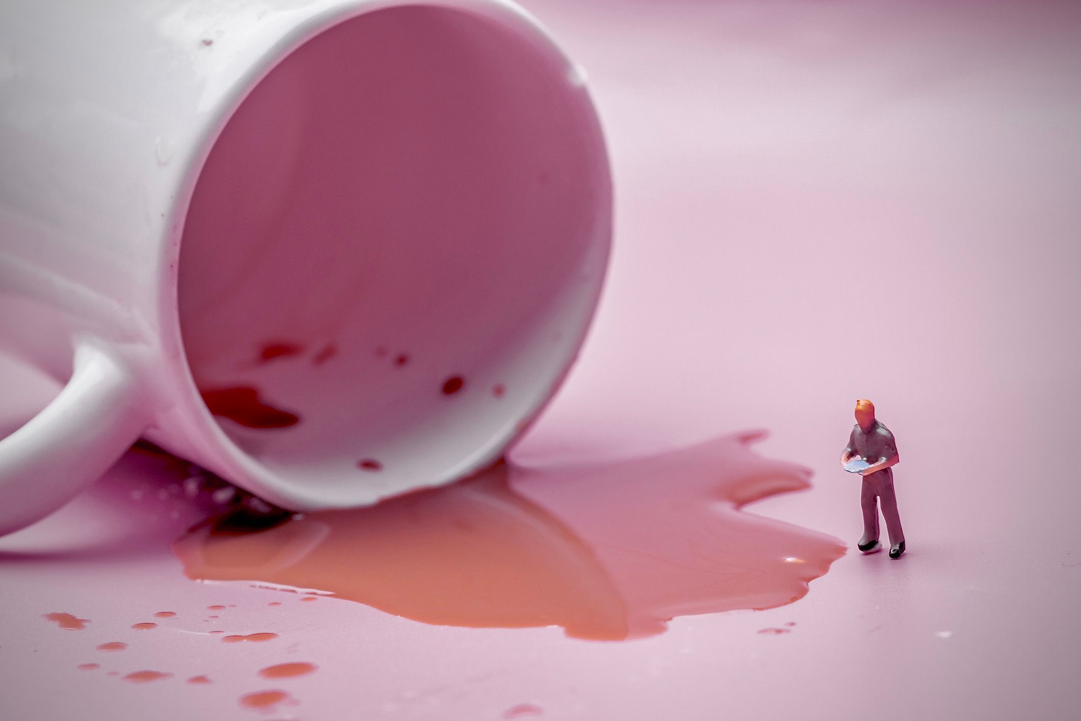 Ein Bild einer menschlichen Miniaturfigur, die verschütteten Kaffee aus einem umgekippten Becher begutachtet.