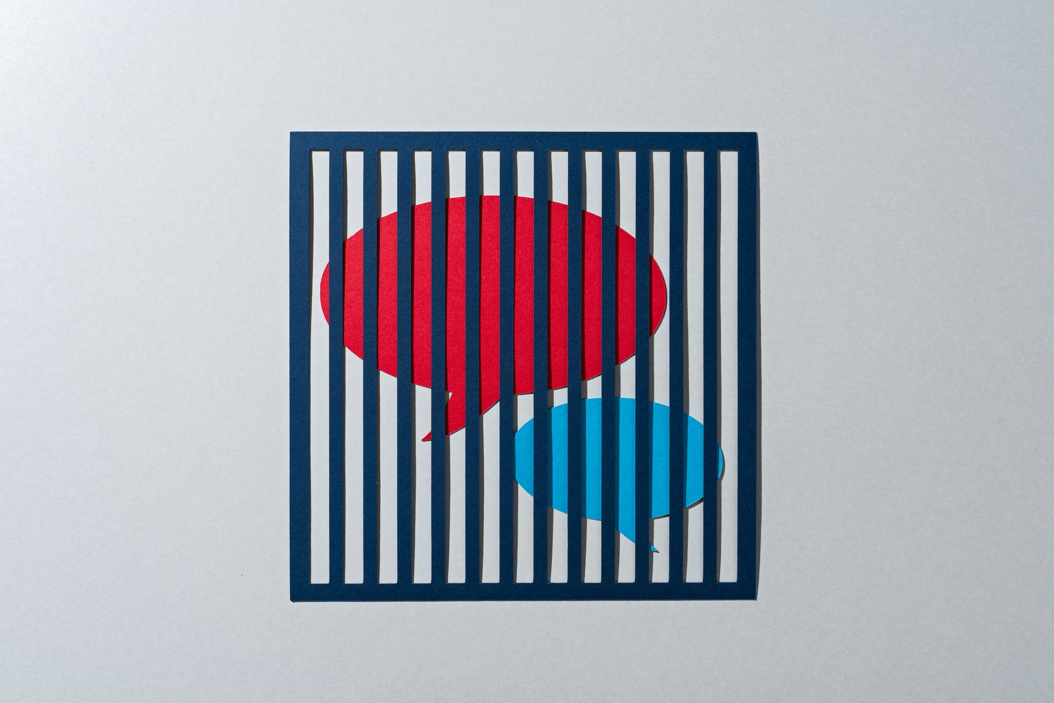 Zwei Sprechblasen, eine rote und eine türkisfarbene, sitzen hinter Gittern gefangen.