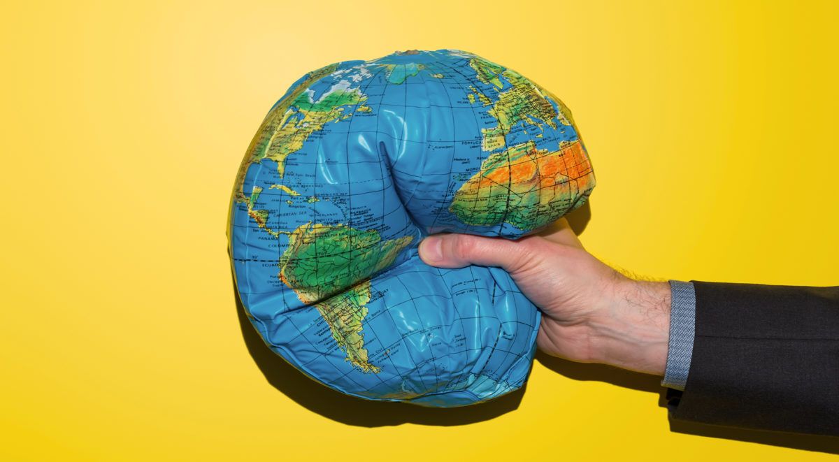 Eine Hand, die einen blauen und grünen Globus vor einem leuchtend gelben Hintergrund hält